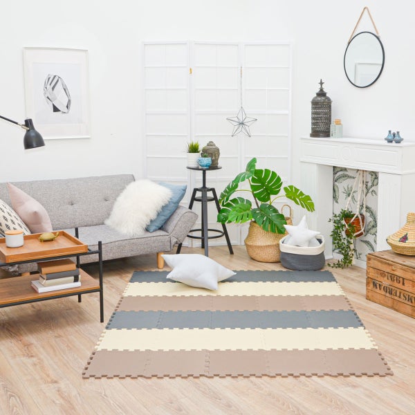 Gestreifte Puzzlematte für den Boden in einem hellen, modernen Wohnzimmer mit grauem Sofa, Holzmöbeln und Zimmerpflanzen.