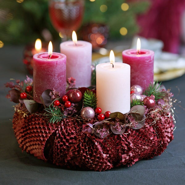Festlicher Adventskranz mit vier brennenden Stumpenkerzen geschmückt mit Tannen grüne Zweigen Beeren und Weihnachtskugeln als Tischdekoration.