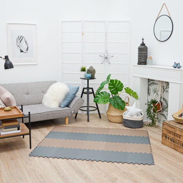 Puzzlematten aus Schaumstoff in Beige und Grau auf hellem Holzboden in einem modern eingerichteten Wohnzimmer mit Sofa und Pflanzen.