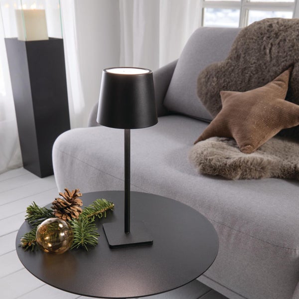 Moderne LED Tischleuchte auf einem runden Beistelltisch in einem gemütlich eingerichteten Wohnbereich mit Sofa und winterlicher Dekoration.