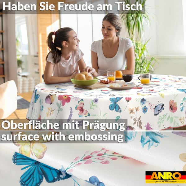 Rundes weißes Tischtuch mit buntem Blumen- und Schmetterlingsmuster auf einem Tisch mit Frau und Kind, inklusive Detailansicht der Prägung.