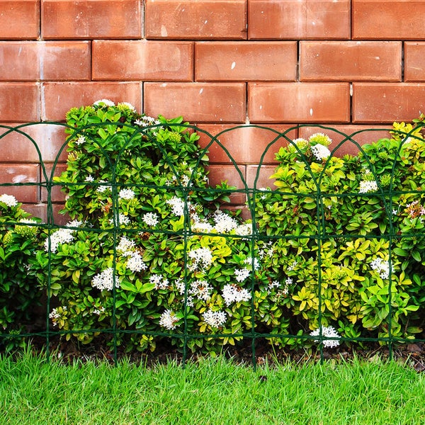 Dunkelgrüner Gartenzaun aus Metall als Beetumrandung vor Sträuchern mit weißen Blüten und einer Ziegelwand.