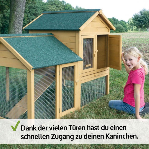 Zweistöckiger Kaninchenstall aus Holz mit Freilaufgehege, Rampe und vielen Türen für schnellen Zugang. Ein Kind sitzt daneben im Garten.
