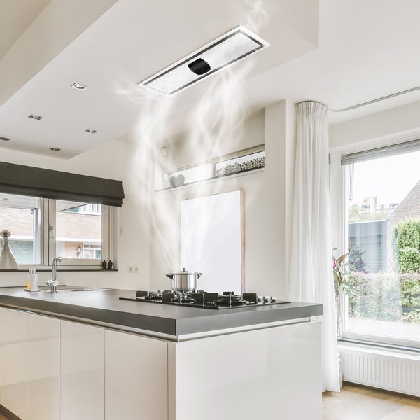 Moderne helle Küche mit Decken-Dunstabzugshaube über einer Kochinsel und Dampf aufsteigend vom Kochfeld.
