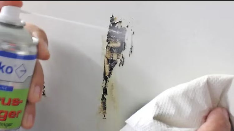 Anwendung eines Reinigungssprays auf Rückständen an einer Oberfläche, eine Hand hält ein Papiertuch bereit.