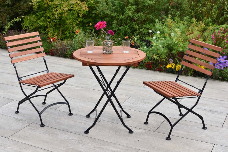 Gartenszene mit einem runden Holztisch und zwei Holzstühlen auf einer Terrasse.