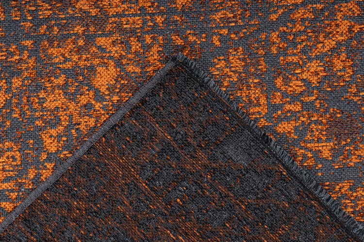 Gewebter Teppich mit abstraktem Muster in Orange und Anthrazit, Nahaufnahme mit umgeknickter Ecke zur Darstellung der Struktur.