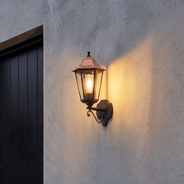 Klassische Außenwandleuchte in Laternenform mit warmem Licht montiert an einer Hausfassade neben einer Tür.