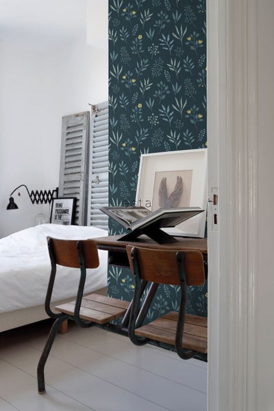 Ein Schlafzimmer mit einer Wandtapete mit Pflanzenmuster, einem Schreibtisch und zwei Stühlen