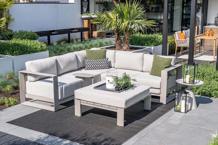 Moderne Eck-Gartenlounge mit hellen Polstern, passendem Couchtisch und dunklem Teppich in einem hellen, gepflegten Außenbereich.