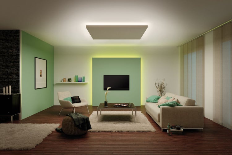 Modernes Wohnzimmer mit großer LED-Deckenleuchte, grüner Akzentwand mit TV, hellem Sofa, dunklem Holzboden und flauschigem Teppich.