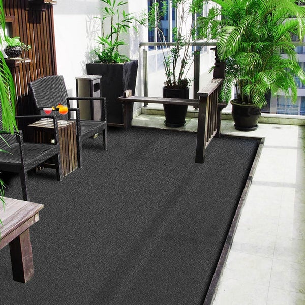 Dunkelgrauer Außenteppich auf einem modernen Balkon mit Polyrattan-Stühlen, Holztisch und verschiedenen Grünpflanzen in Töpfen.