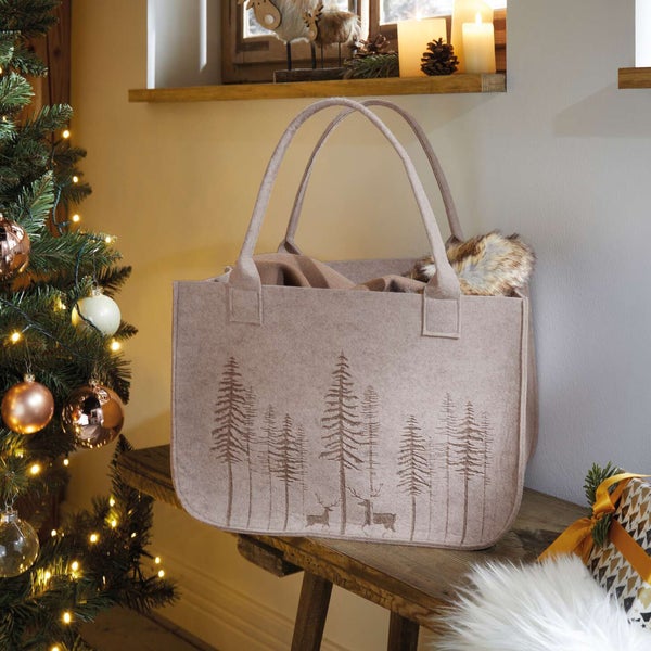 Dekorative Filztasche mit Waldmotiv auf einer Holzbank neben einem Weihnachtsbaum.
