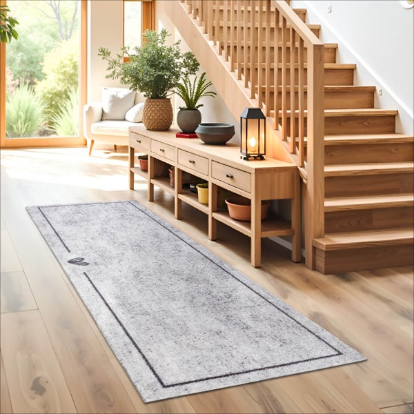 Langer grauer Läufer mit dunklem Rand auf Holzfußboden neben einer Treppe und einem Sideboard aus Holz in einem hellen Flur.