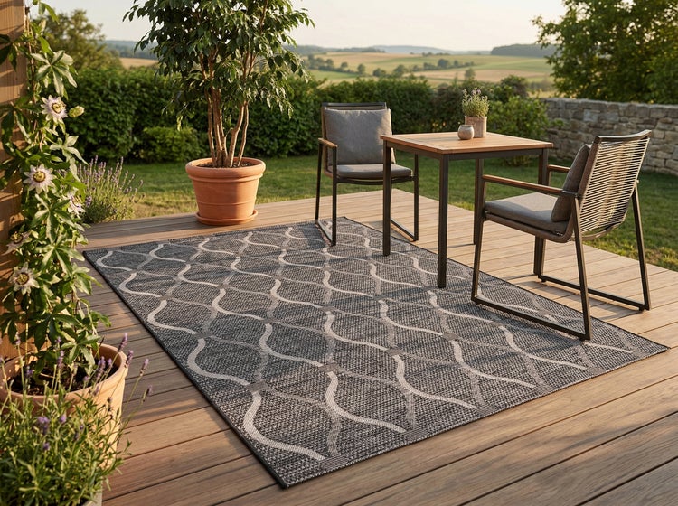 Outdoor Teppich mit geometrischem Muster auf einer Holzterrasse mit Sitzgruppe und Pflanzen in einer ländlichen Gartenumgebung