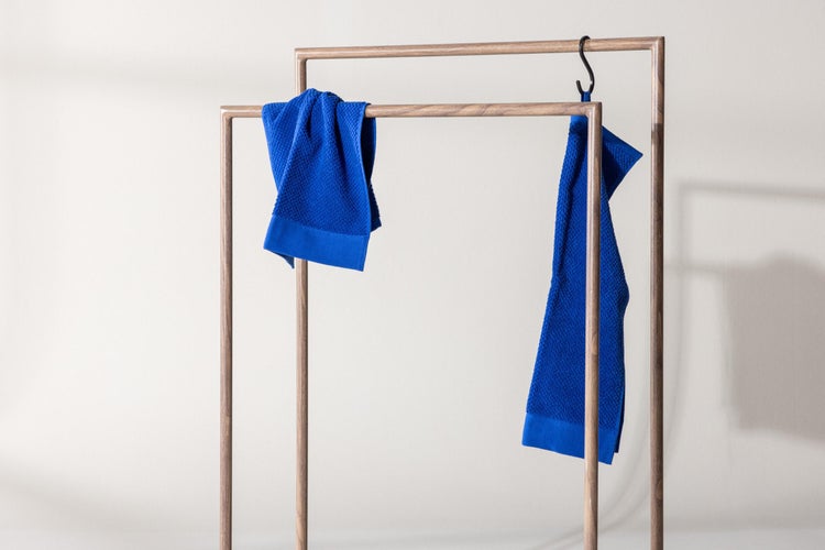 Zwei blaue Handtücher mit Waffelstruktur an einem freistehenden Handtuchhalter aus Holz.