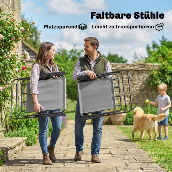 Ein Paar trägt platzsparende und leicht zu transportierende Klappstühle durch einen hellen Garten.