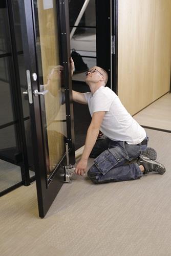 Ein Mann kniet vor einer schwarzen Innentür und befestigt eine Türklinke.