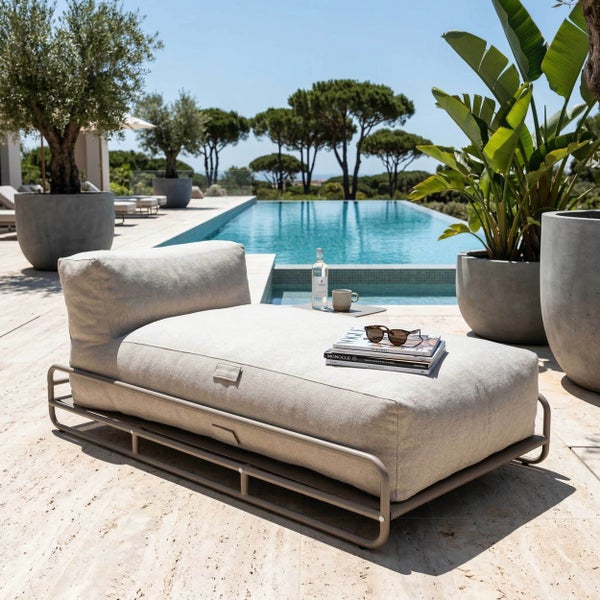 Modernes Outdoor-Liegesofa mit Metallgestell und dickem Polster auf einer hellen Steinterrasse an einem Pool mit mediterranen Pflanzen.