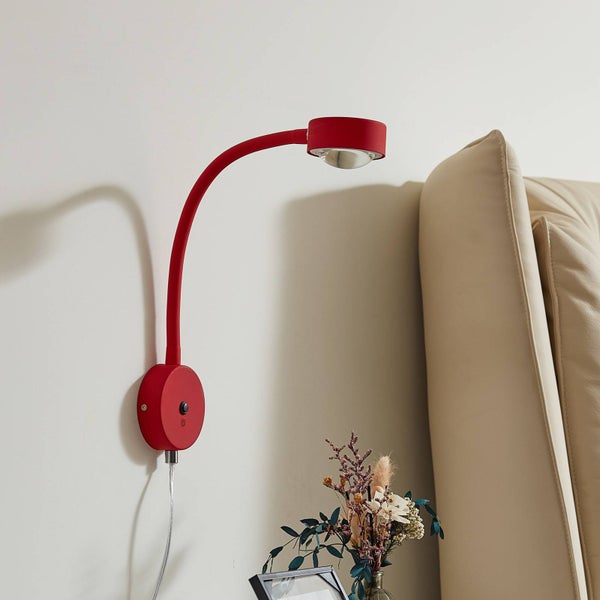 Rote Wandleuchte mit flexiblem Arm neben einem Sofa.