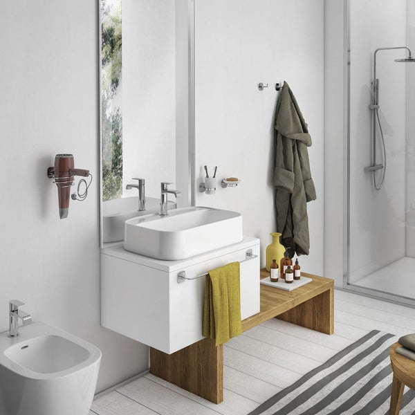 Helles, organisiertes Badezimmer mit weißem Aufsatzwaschbecken, Holzbank, Dusche, Bidet und verchromten Wandaccessoires wie einem Föhnhalter.
