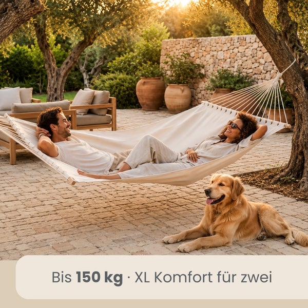 Weiße Doppelhängematte in einem hellen Garten mit Natursteinmauer. Komfort für zwei Personen mit einer Tragkraft bis 150 Kilogramm.