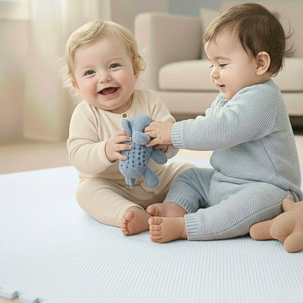Zwei Babys spielen auf einer weichen Puzzlematte in einem hellen Wohnzimmer.