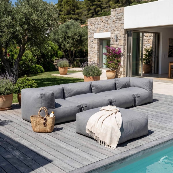 Modernes graues modulares Outdoor Lounge Sofa mit Hocker auf einer Holzterrasse am Pool in einem Garten mit Natursteinwand