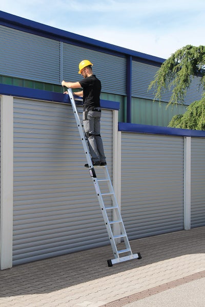 Eine Person mit Schutzhelm steht auf einer Anlegeleiter vor einem Gebäude.
