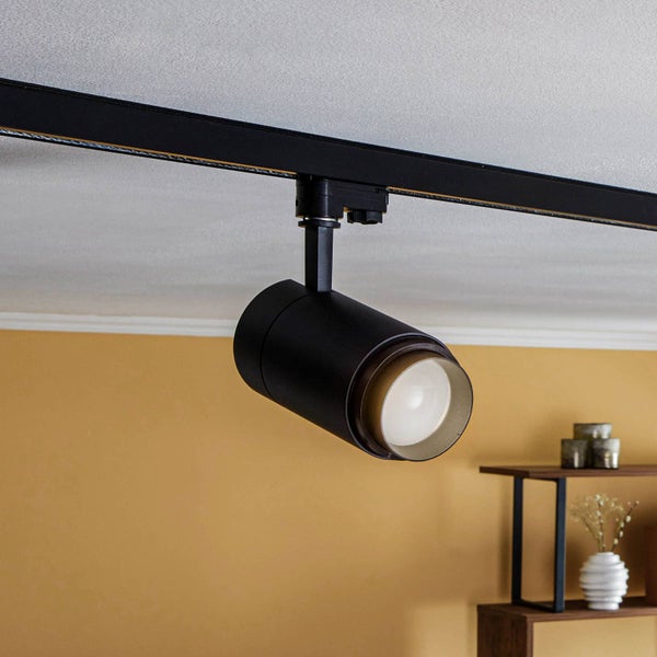 Schwarzer Strahler für ein Schienensystem, montiert an der Decke in einem modern eingerichteten Raum vor einer gelben Wand.