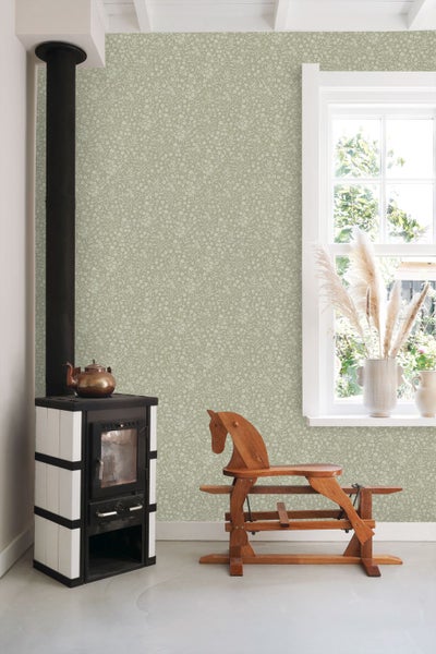 Helles Zimmer mit gemusterter Blumentapete, Kaminofen mit Teekessel und einem hölzernen Schaukelpferd vor der Wand.