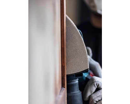 Eine Person schleift mit einem Deltaschleifer ein Holzprodukt.