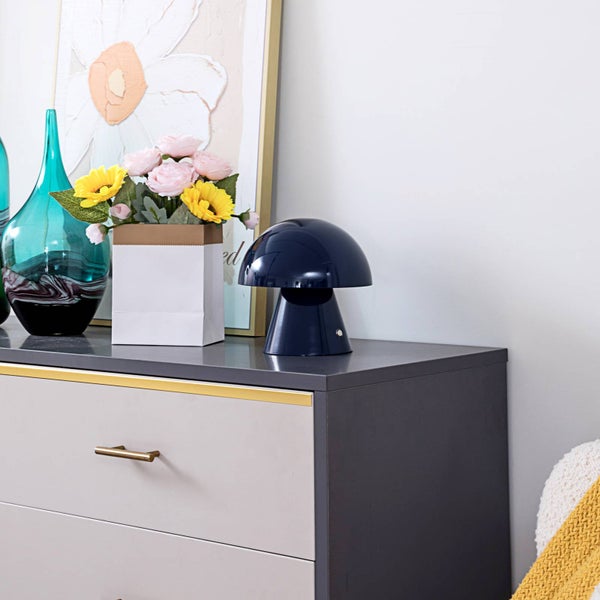 Pilzförmige Tischleuchte auf einer Kommode neben Blumen und einer Glasvase in einem hell gestalteten Raum.