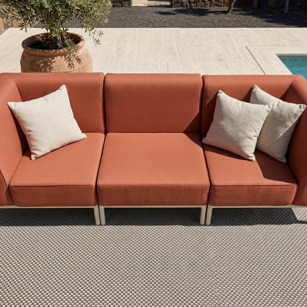 Modernes 3-Sitzer Gartensofa in Terracotta mit hellen Kissen auf einer hellen Terrasse mit Outdoor-Teppich, Steinboden und Pool.