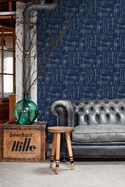 Wohnraum mit blau gemusterter Flugzeugtapete, Leder-Sofa und Holzhocker