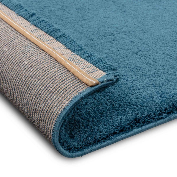Nahaufnahme einer blauen Teppichecke mit flauschiger Oberfläche und gewebter Rückseite.