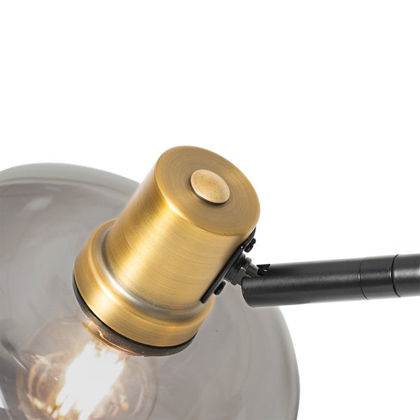 Detailansicht einer Lampe mit einer Fassung in Messingoptik, einem schwarzen Gelenkarm und einem runden Schirm aus Rauchglas.