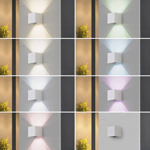 Würfelförmige Außenwandleuchte mit LED-Licht nach oben und unten in verschiedenen RGB-Farben an einer grauen Fassade.
