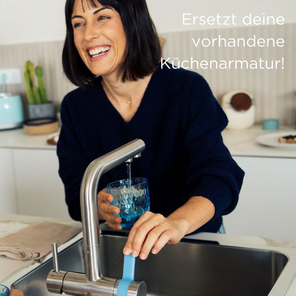 Eine Frau füllt ein Glas Wasser an einer modernen Küchenarmatur aus Edelstahl über einem Spülbecken in einer hellen Küche auf.