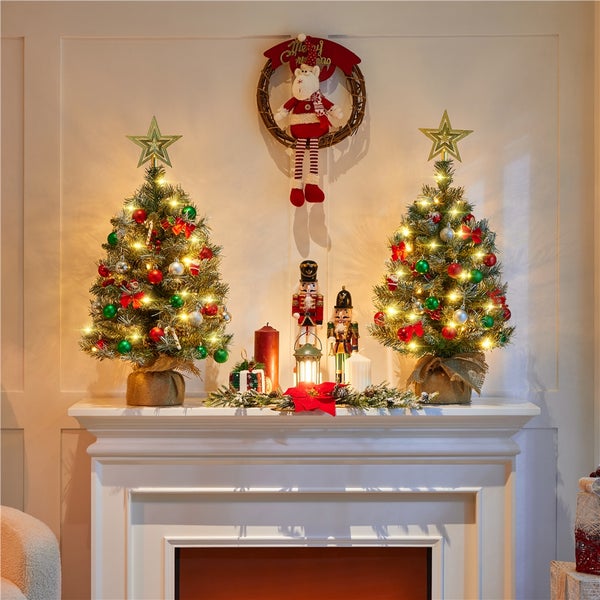 Weihnachtliche Dekoration mit zwei kleinen Weihnachtsbäumen, Nussknackern und Kranz auf einem Kaminsims