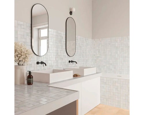 Modernes helles Badezimmer mit Doppelwaschtisch, Aufsatzbecken, Wandarmaturen, ovalen Spiegeln und Mosaikfliesen im Flechtmuster.