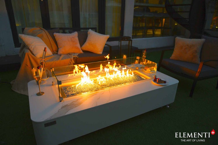 Rechteckiger Gaskamin-Tisch mit Marmordekor, Glas-Windschutz und brennenden Flammen in einer modern eingerichteten Gartenlounge.