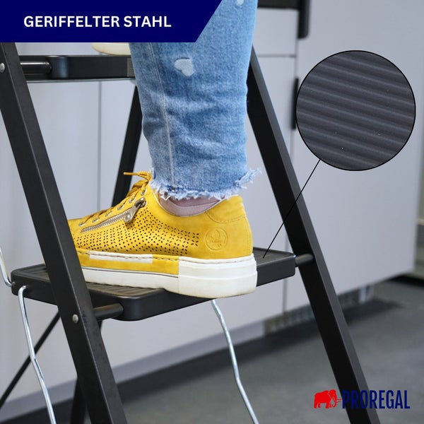 Trittleiter aus schwarzem Stahl mit geriffelter Trittfläche für besseren Halt. Detailansicht der Oberflächenstruktur und Proregal Logo.