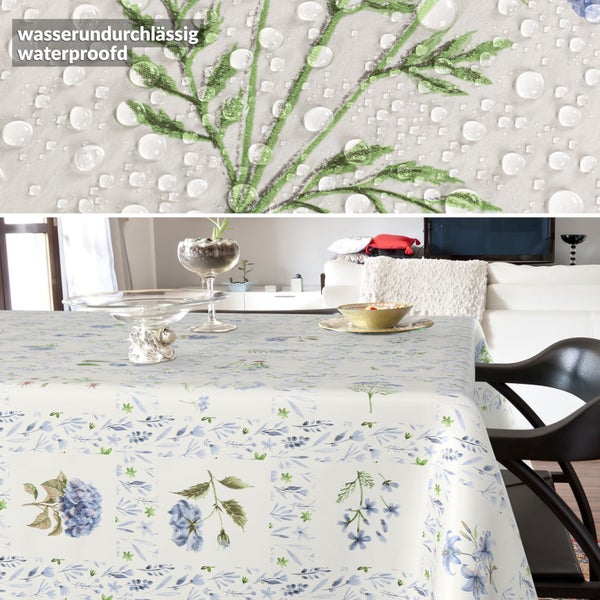 Wasserundurchlässige Tischdecke mit floralem Muster aus blauen Blumen und grünen Zweigen in einem hellen Wohnzimmer.