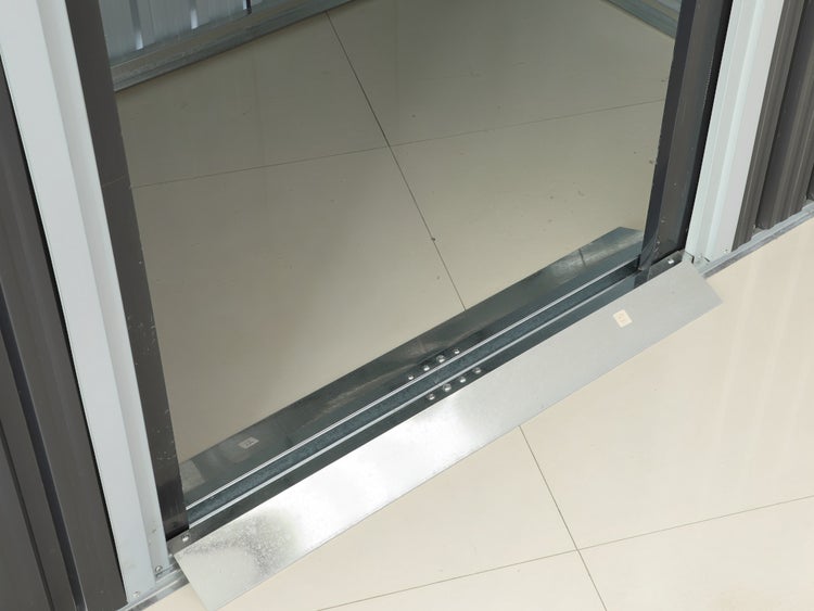 Silberfarbene Metallrampe an der Türschwelle eines dunkelgrauen Gerätehauses aus Metall.