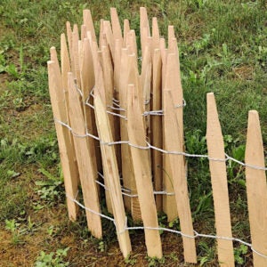 Staketenzaun aus Holzlatten, verbunden mit Draht, auf einer Wiese stehend.