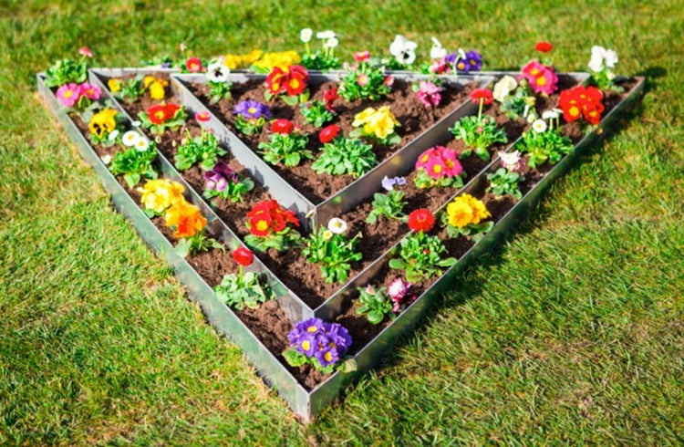 Beetbegrenzung in Dreiecksform mit bunten Blumen auf einer Rasenfläche