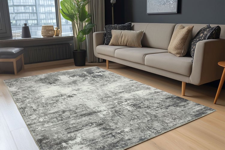 Moderner Wohnbereich mit einem grauen Teppich mit abstraktem Muster, hellem Sofa, Zimmerpflanze und Parkettboden.