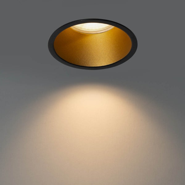 Runder Einbaustrahler mit schwarzem Gehäuse und goldfarbenem Reflektor im eingeschalteten Zustand.