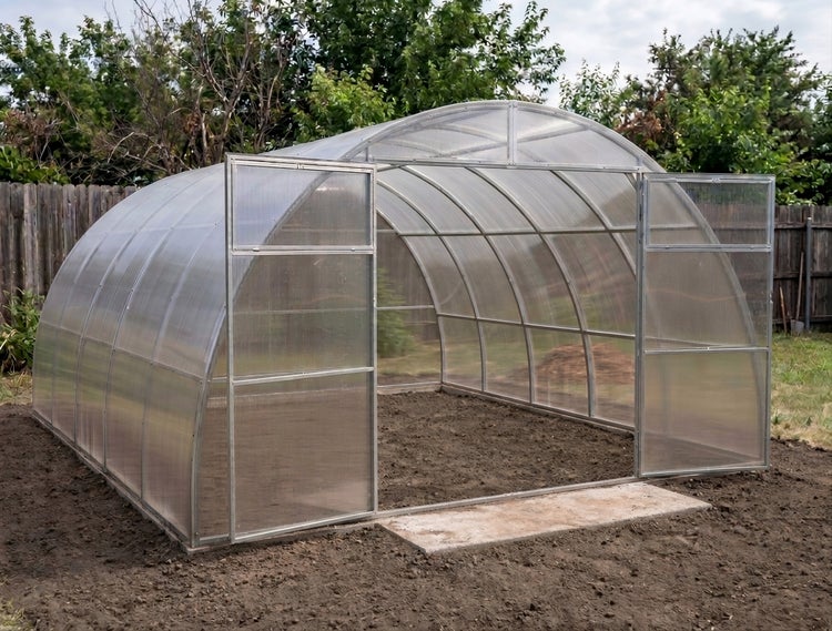 Tunnelförmiges Gewächshaus mit Metallrahmen und transparenten Stegplatten im Garten mit geöffneten Doppeltüren auf dem Erdboden.